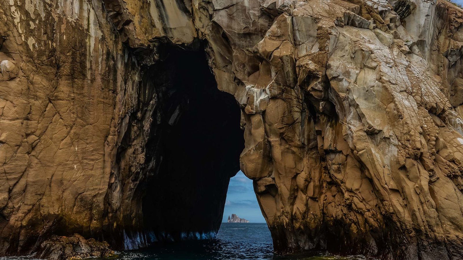 Entrada a una cueva marina en acantilados de roca volcánica en Galápagos con vista al mar abierto.